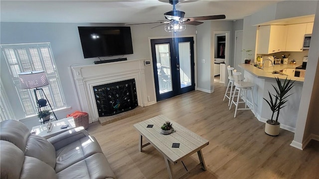 living room with light wood-style floors, baseboards, a fireplace with raised hearth, and french doors