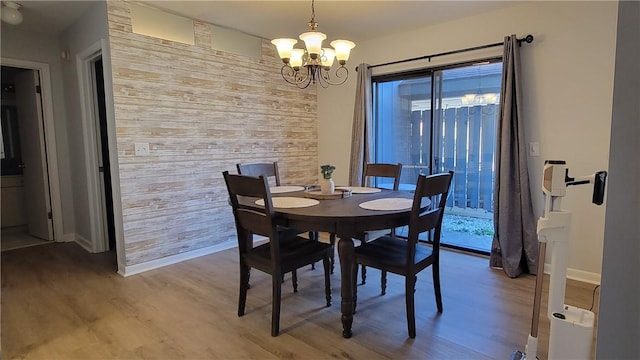 dining area featuring baseboards, an accent wall, wood walls, light wood-style floors, and a chandelier