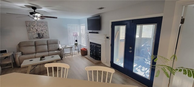 living area featuring a fireplace with raised hearth, ceiling fan, visible vents, and light wood-style floors