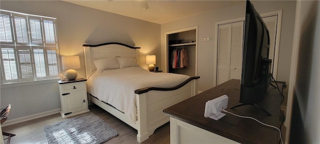 bedroom featuring multiple closets, baseboards, and wood finished floors