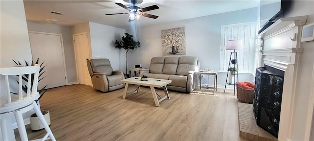 sitting room with ceiling fan, a brick fireplace, wood finished floors, and visible vents