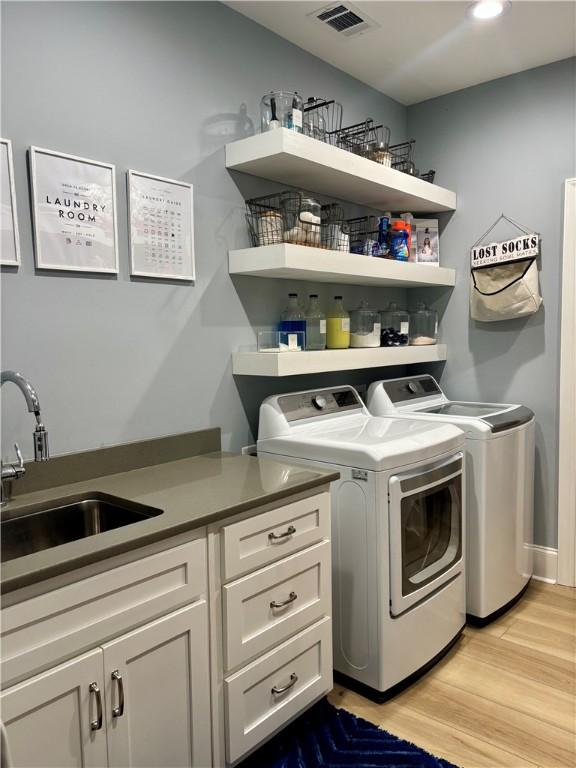 washroom featuring light wood-style flooring, visible vents, a sink, and independent washer and dryer