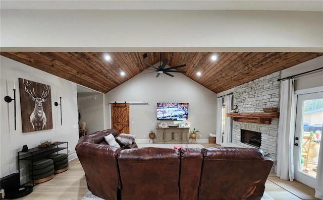 living room with a barn door, a ceiling fan, wood ceiling, a stone fireplace, and light wood-style floors