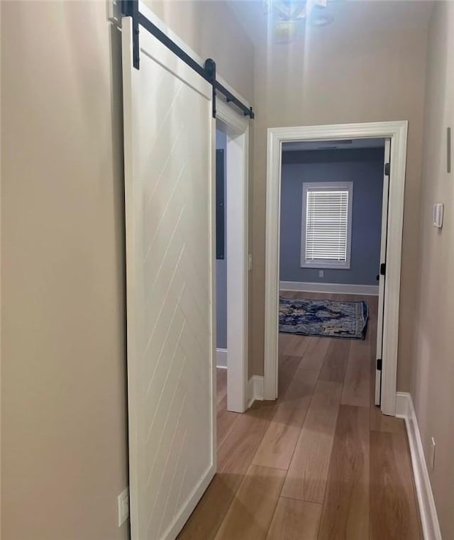 hall featuring light wood finished floors, a barn door, and baseboards