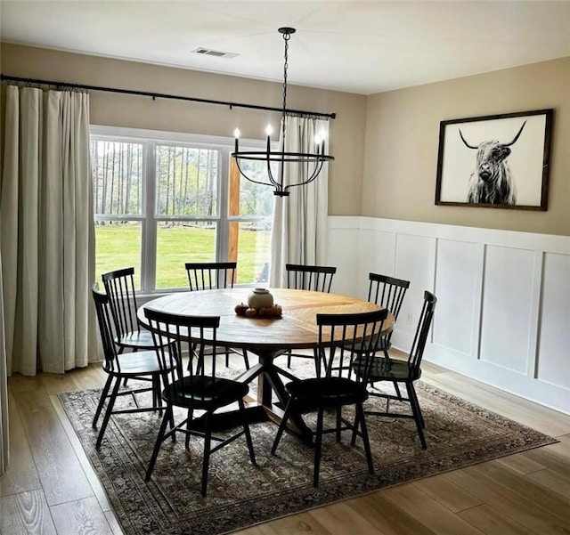 dining room with a wainscoted wall, visible vents, a decorative wall, light wood-style floors, and a chandelier