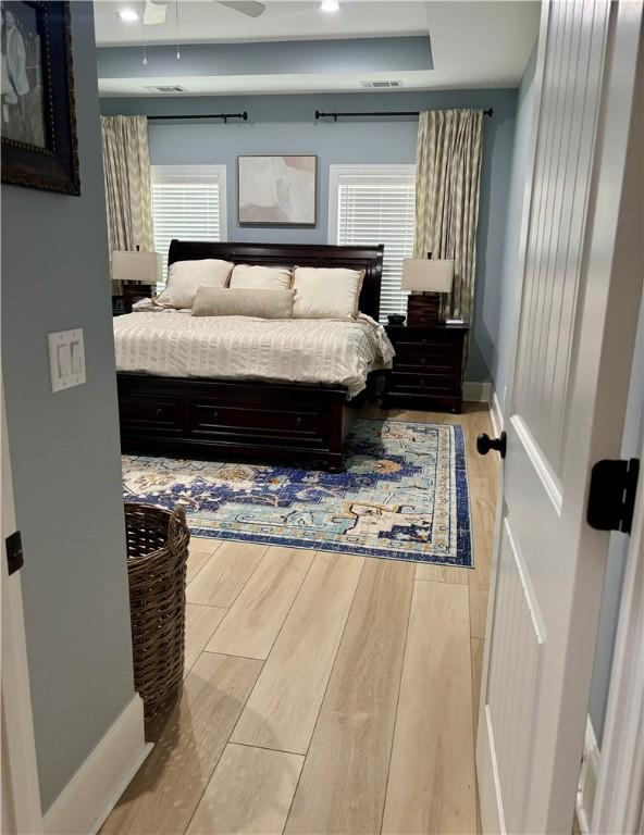 bedroom with visible vents, baseboards, a raised ceiling, and wood finished floors