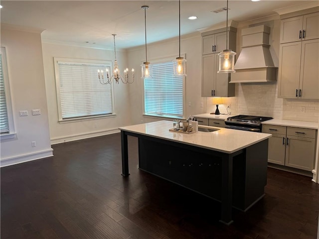 kitchen with sink, stainless steel gas range oven, premium range hood, decorative light fixtures, and a kitchen island with sink