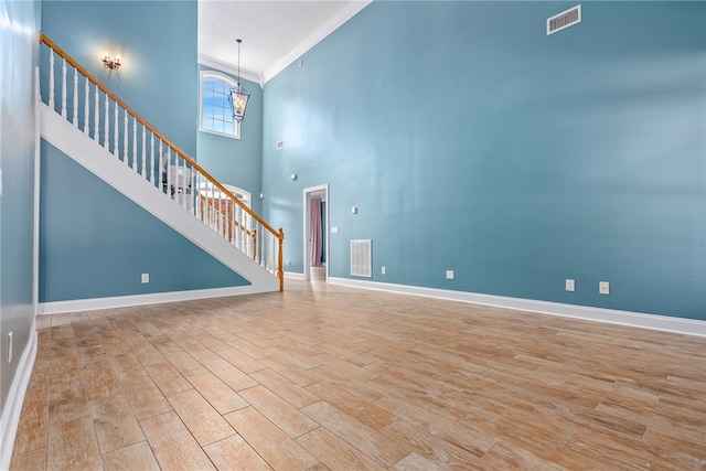 unfurnished living room with crown molding, light hardwood / wood-style flooring, a chandelier, and a high ceiling