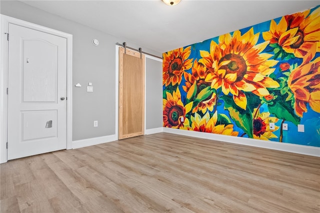 unfurnished room with a barn door and light wood-type flooring