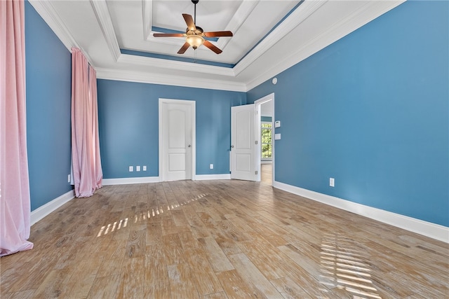 empty room featuring ceiling fan, light wood-type flooring, crown molding, and a tray ceiling