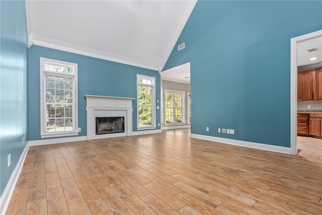 unfurnished living room with plenty of natural light, light hardwood / wood-style floors, crown molding, and high vaulted ceiling