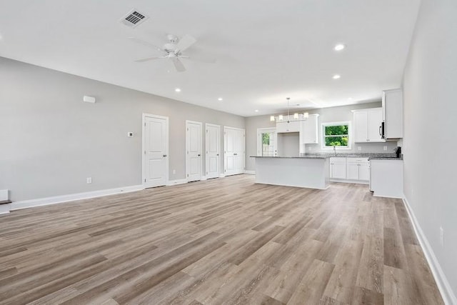 unfurnished living room featuring ceiling fan with notable chandelier and light hardwood / wood-style floors