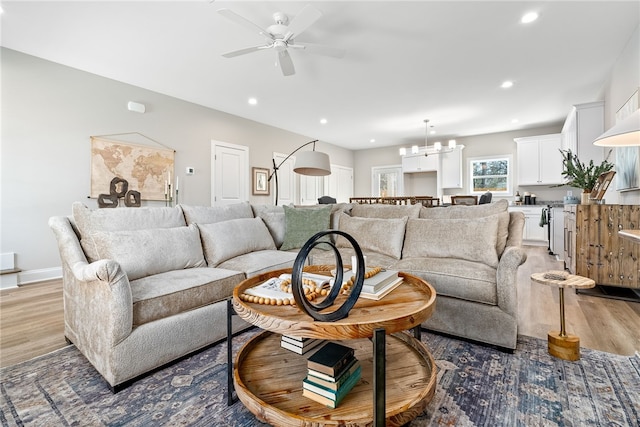 living area featuring recessed lighting, ceiling fan with notable chandelier, baseboards, and light wood-type flooring