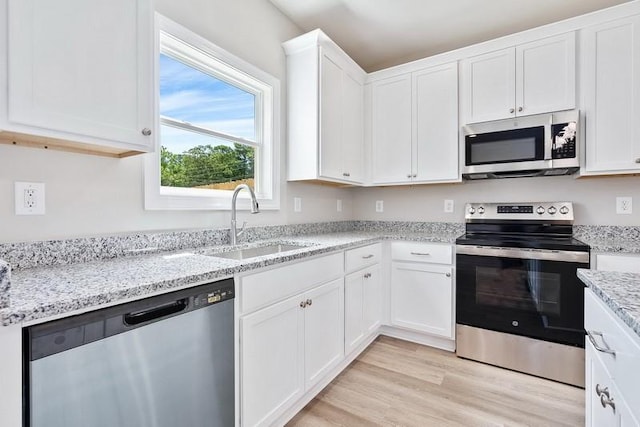 kitchen featuring white cabinetry, sink, stainless steel appliances, and light stone counters