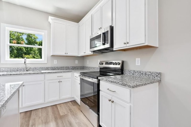 kitchen featuring light stone countertops, appliances with stainless steel finishes, light wood-type flooring, sink, and white cabinetry