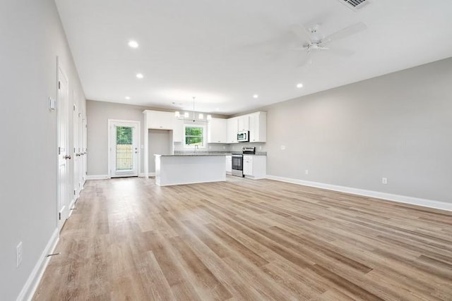 unfurnished living room with ceiling fan with notable chandelier and light wood-type flooring