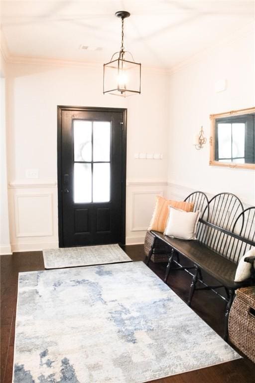 entrance foyer featuring an inviting chandelier, dark wood-type flooring, and ornamental molding