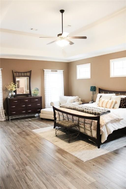 bedroom featuring ceiling fan, ornamental molding, a raised ceiling, and light hardwood / wood-style floors