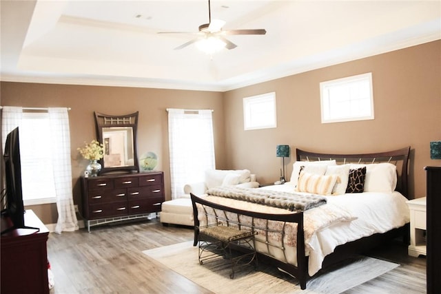 bedroom featuring crown molding, a raised ceiling, ceiling fan, and light wood-type flooring