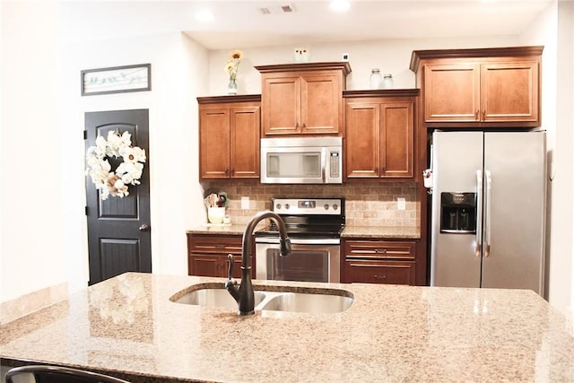 kitchen with tasteful backsplash, appliances with stainless steel finishes, light stone countertops, and sink