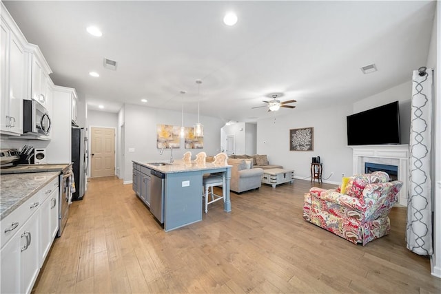 kitchen featuring visible vents, a breakfast bar, open floor plan, stainless steel appliances, and white cabinets