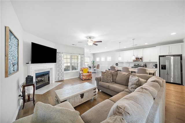 living room featuring wood finished floors, baseboards, a premium fireplace, recessed lighting, and ceiling fan