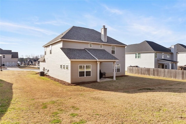 rear view of property featuring central AC unit, fence, a shingled roof, a chimney, and a lawn