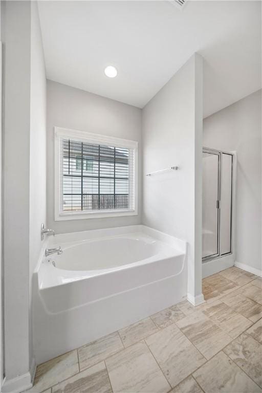 full bathroom with baseboards, a garden tub, and a shower stall