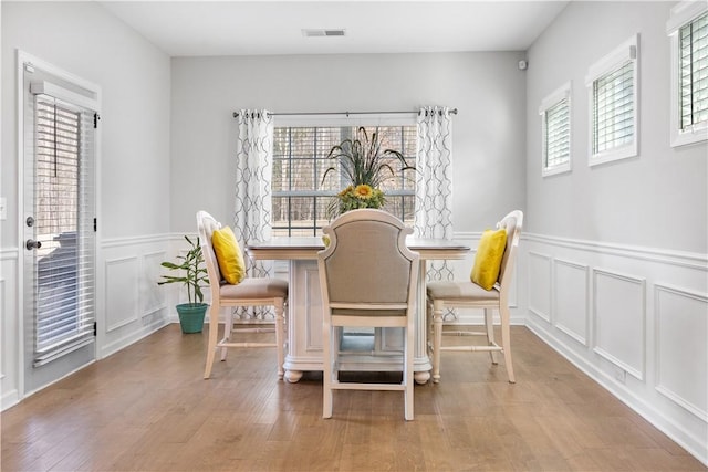 dining area with visible vents, wood finished floors, wainscoting, and a decorative wall