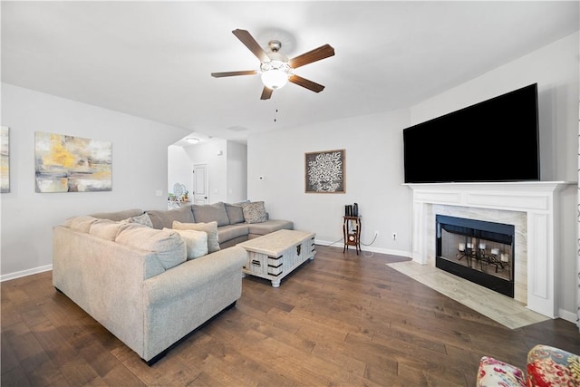 living room with a tiled fireplace, a ceiling fan, dark wood-type flooring, and baseboards