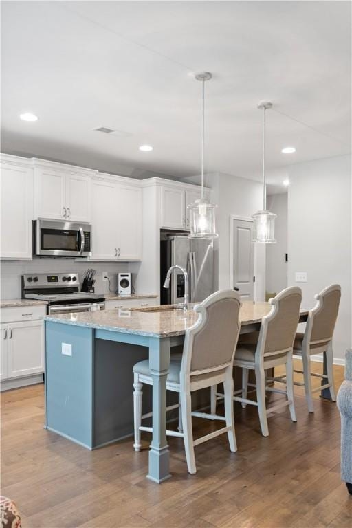 kitchen with an island with sink, a kitchen breakfast bar, stainless steel appliances, light wood-style floors, and white cabinets