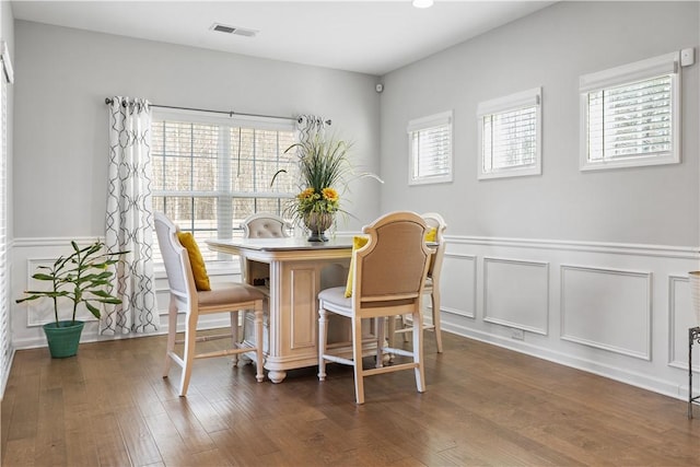 dining space with a wealth of natural light, visible vents, dark wood finished floors, and a decorative wall