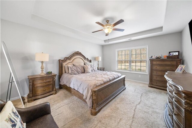 bedroom featuring light carpet, ceiling fan, a raised ceiling, and baseboards