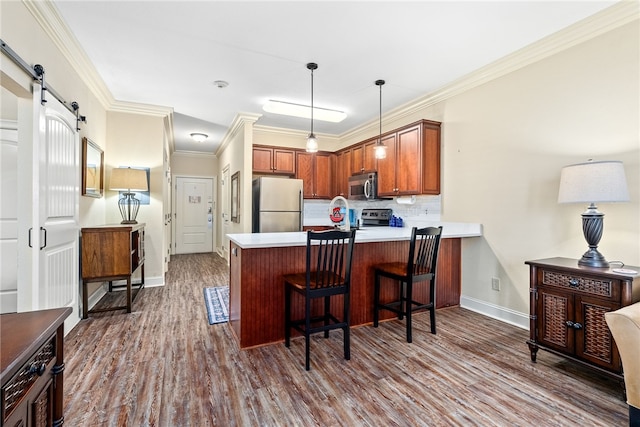 kitchen featuring dark wood finished floors, decorative backsplash, a barn door, appliances with stainless steel finishes, and a peninsula