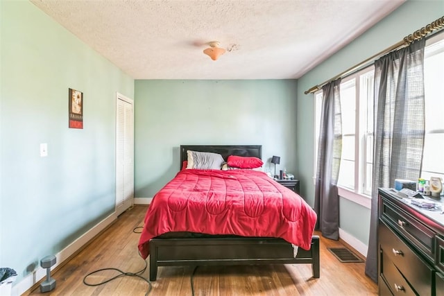 bedroom featuring a textured ceiling, light hardwood / wood-style floors, and multiple windows