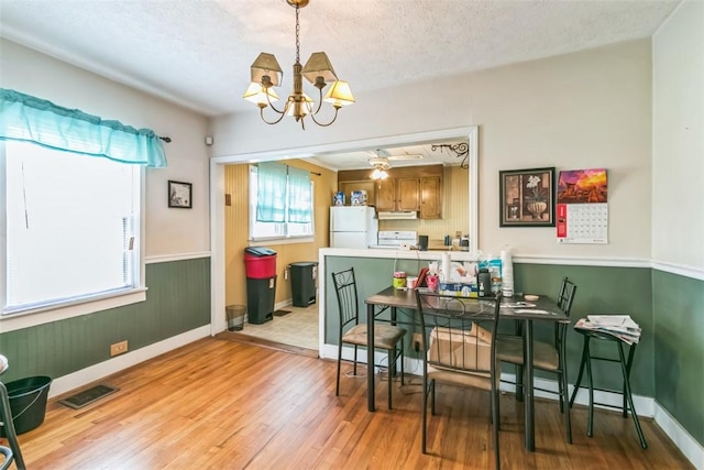 dining space featuring light wood-type flooring, a textured ceiling, and ceiling fan with notable chandelier