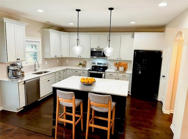 kitchen with a kitchen island, dark wood-type flooring, stainless steel appliances, white cabinetry, and a sink