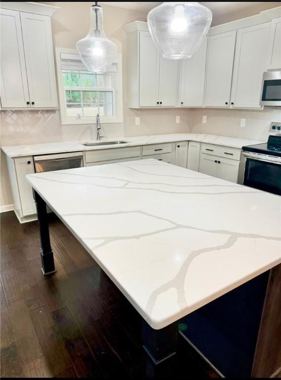 kitchen with light stone counters, a kitchen island, a sink, appliances with stainless steel finishes, and dark wood-style floors