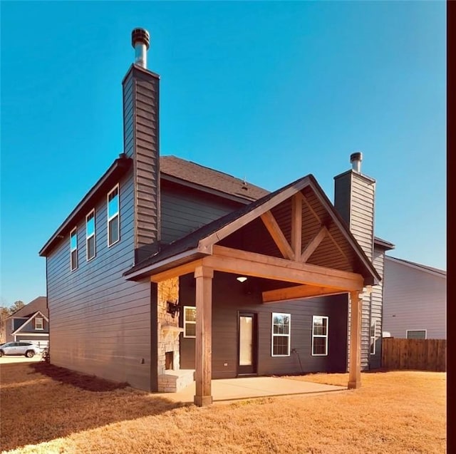 rear view of house featuring a patio area, a chimney, fence, and stone siding