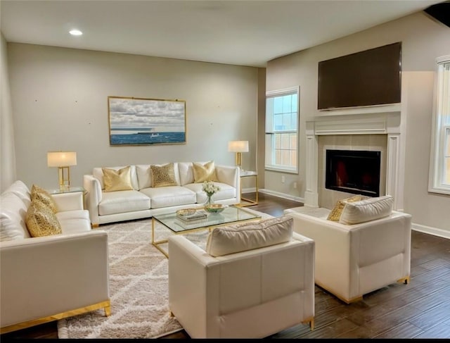 living room with dark wood-type flooring, a tiled fireplace, recessed lighting, and baseboards