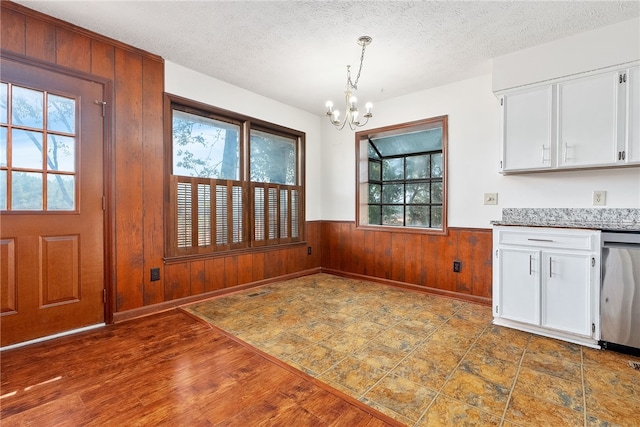 unfurnished dining area featuring a textured ceiling, a wealth of natural light, wooden walls, and a notable chandelier