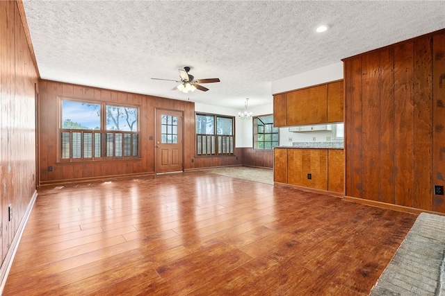 unfurnished living room with a textured ceiling, ceiling fan with notable chandelier, hardwood / wood-style flooring, and wood walls