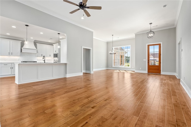 unfurnished living room with light wood finished floors, ornamental molding, a sink, and ceiling fan with notable chandelier