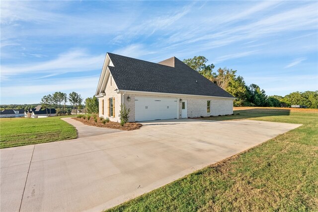 view of side of property featuring driveway, a garage, roof with shingles, a yard, and brick siding