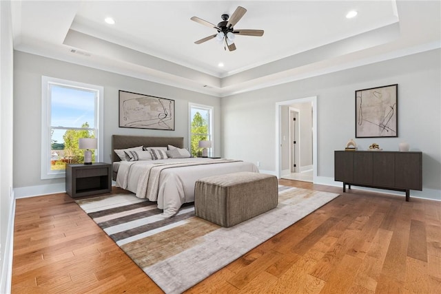 bedroom featuring light wood-style floors, a tray ceiling, visible vents, and baseboards