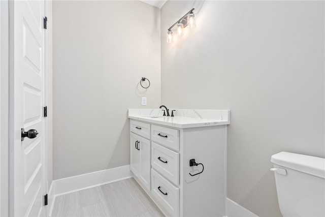 half bath featuring baseboards, vanity, and toilet