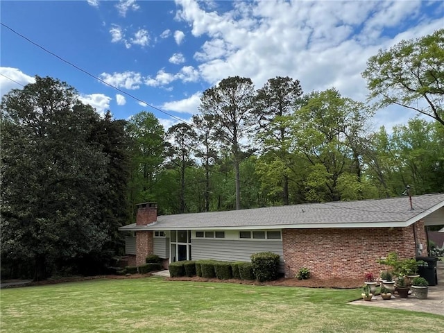 view of front of house featuring brick siding, a chimney, a patio area, and a front yard