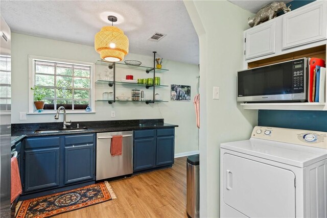 kitchen with a sink, blue cabinetry, washer / dryer, stainless steel dishwasher, and visible vents