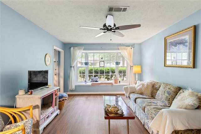 living room with a textured ceiling, a ceiling fan, baseboards, wood finished floors, and visible vents
