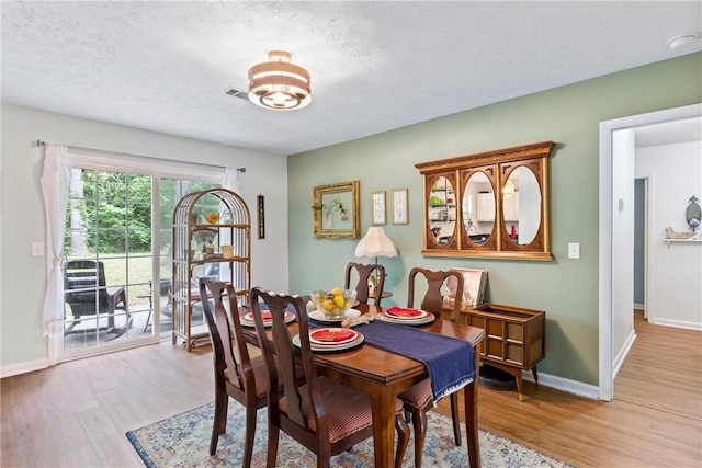 dining area with a textured ceiling, baseboards, visible vents, and light wood-style flooring
